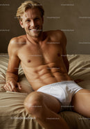 Smiling young man relaxing on bed in white underwear