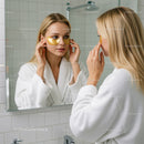 Woman in a White Bathrobe Applying Eye Mask in Mirror Reflection