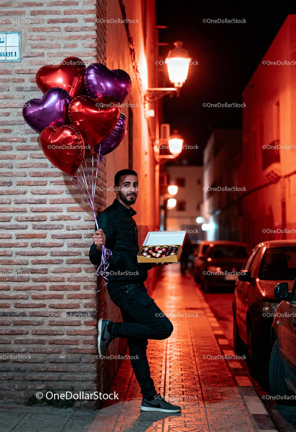 Man holding heart balloons and chocolates on romantic night
