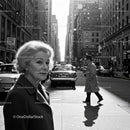 Elderly Woman in Busy City Street Surrounded by Vintage Cars