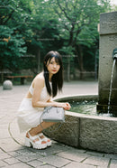 Young Woman in White Dress with Gray Handbag at City Park Fountain