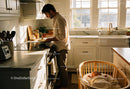 Father Preparing Breakfast While Baby Sleeps Nearby