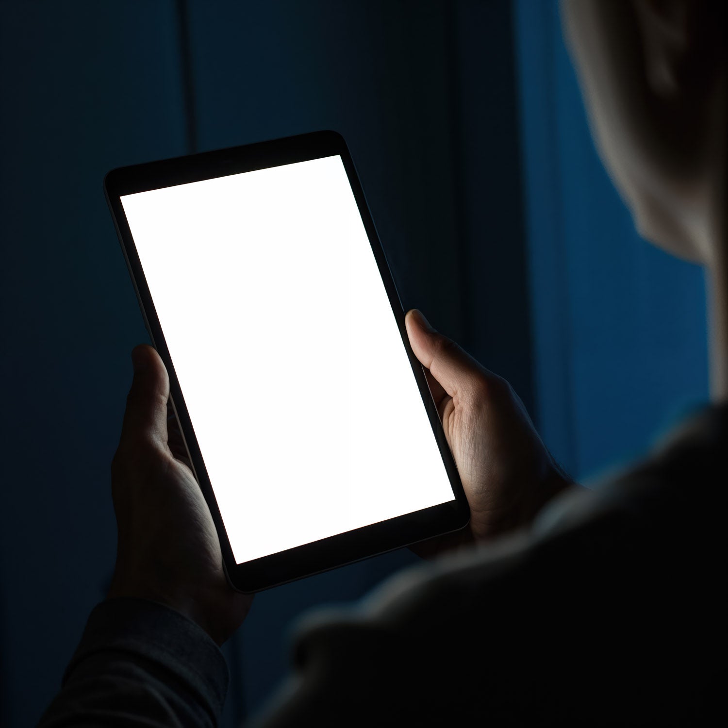 Osoba trzymająca jasny tablet w ciemnym pomieszczeniu