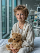 Smiling Young Child Sitting on Hospital Bed with Teddy Bear