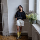 Casual Young Woman in Black T-Shirt and Beige Shorts in Indoor Setting