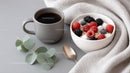 Fresh Fruit and Yogurt in White Bowl with Coffee on Cozy Table