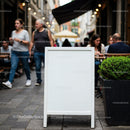 Blank sidewalk sign outside bustling city cafe