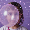 Child gazing through transparent balloon with bokeh lights