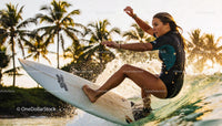 Young Woman Surfing a Wave at Sunset with Palm Trees