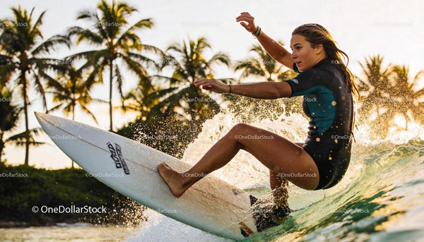 Young Woman Surfing a Wave at Sunset with Palm Trees