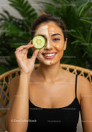 Smiling Woman with Facial Mask and Cucumber in Lush Green Setting