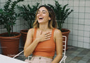 Joyful Young Woman in Orange Top Laughing with Potted Plants in Modern Indoor Garden