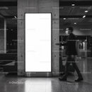 Blurred man walking past large illuminated billboard indoors