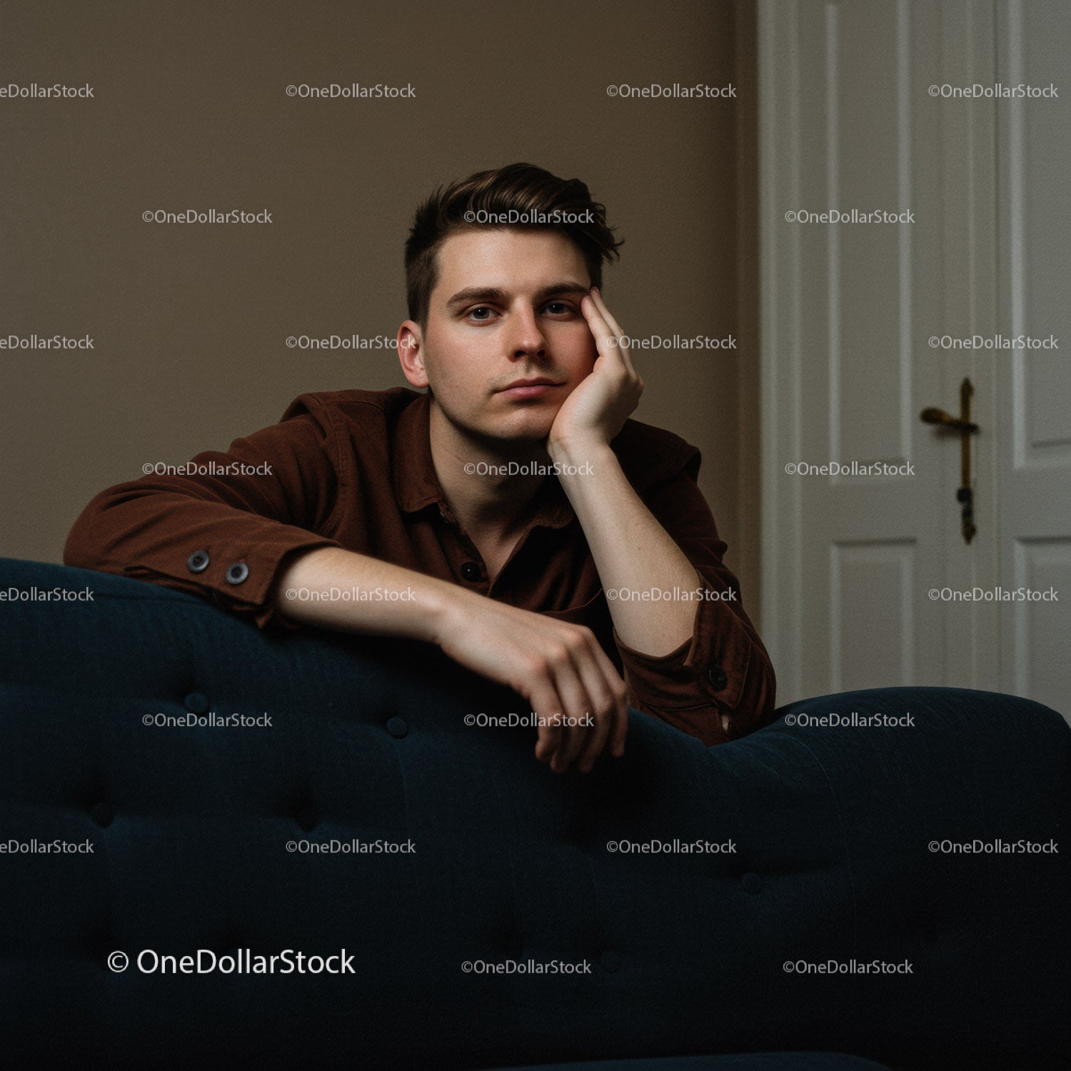 Młody mężczyzna siedzący na sofie z zamyślonym wyrazem twarzy w nowoczesnym wnętrzu