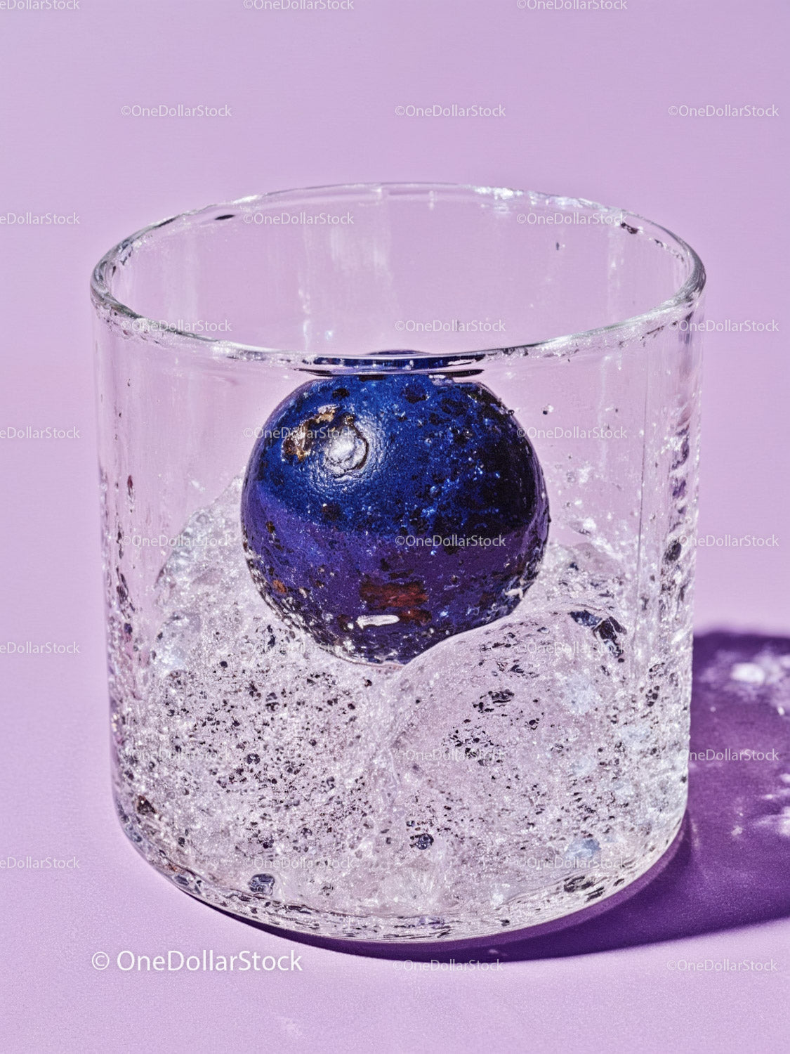 Blueberry immersed in sparkling water in glass on purple