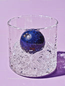 Blueberry immersed in sparkling water in glass on purple