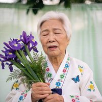 Elderly woman in traditional dress holding flowers with eyes closed