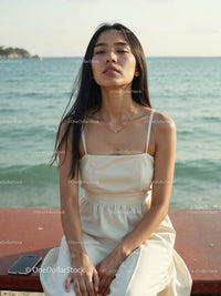 Elegant Woman in White Dress Sitting by Relaxing Seaside Landscape