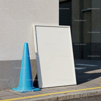 Blank white frame leaning on wall near blue traffic cone