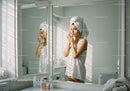 Woman Applying Face Cream in Bright Bathroom with Mirror Reflection