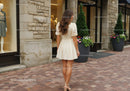 Fashionable Woman in Beige Dress Walking Past Storefront with Flower Pots