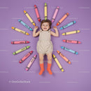 Happy toddler surrounded by colorful giant crayons on purple