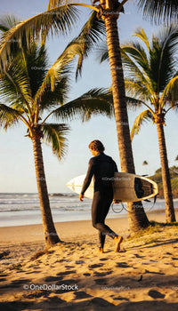 Surfer walking on tropical beach at sunset with surfboard