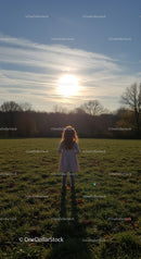 Child standing in sunlit field at sunset