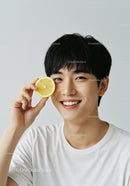Happy Young Man Holding Lemon Slice with Bright Smile in Casual Setting