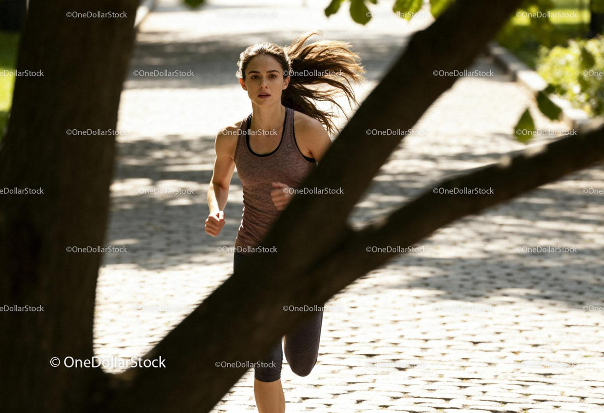 Focused woman running through sunny park path
