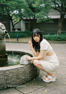 Young Woman in White Embroidered Dress Sitting by Water Fountain in Park