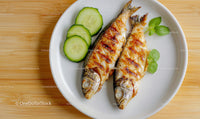 Grilled Sardines with Cucumber Slices and Fresh Herbs on White Plate