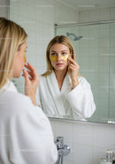 Young Woman Applying Eye Patches in Bathroom Mirror