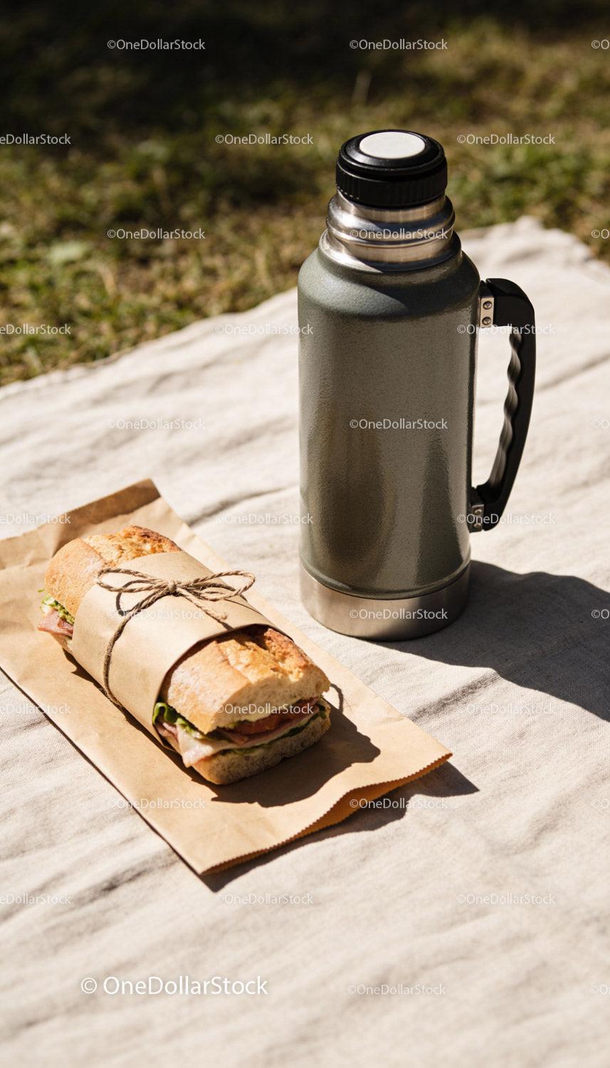 Packed sandwich and thermos flask on picnic blanket