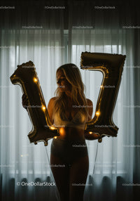 Woman holding illuminated gold 17 balloons indoors