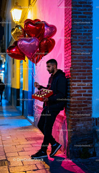 Young man with heart balloons and chocolates on street