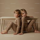 Two children sitting back to back in cozy neutral clothes