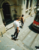 Young Man Skateboarding and Woman Walking on City Street