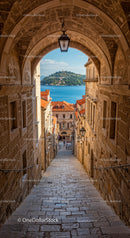 Scenic Coastal Town View through Stone Arch with Orange Rooftops and Seaside Landscape
