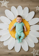 Smiling baby lying on large artificial daisy flower mat