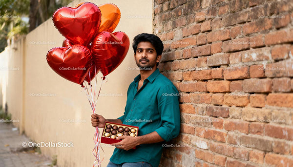 Young man holding heart balloons and chocolates outdoors