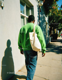 Young Man in Green Sweater with Canvas Bag Walking on Sunny City Sidewalk