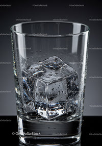 Close up of clear glass with single ice cube and water droplets