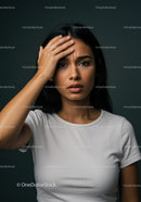 Woman with Worried Expression Touching Forehead Against Dark Background