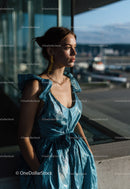 Young Woman in Blue Metallic Dress Near Large Glass Window at Airport