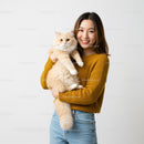 Young woman holding fluffy ginger cat indoors