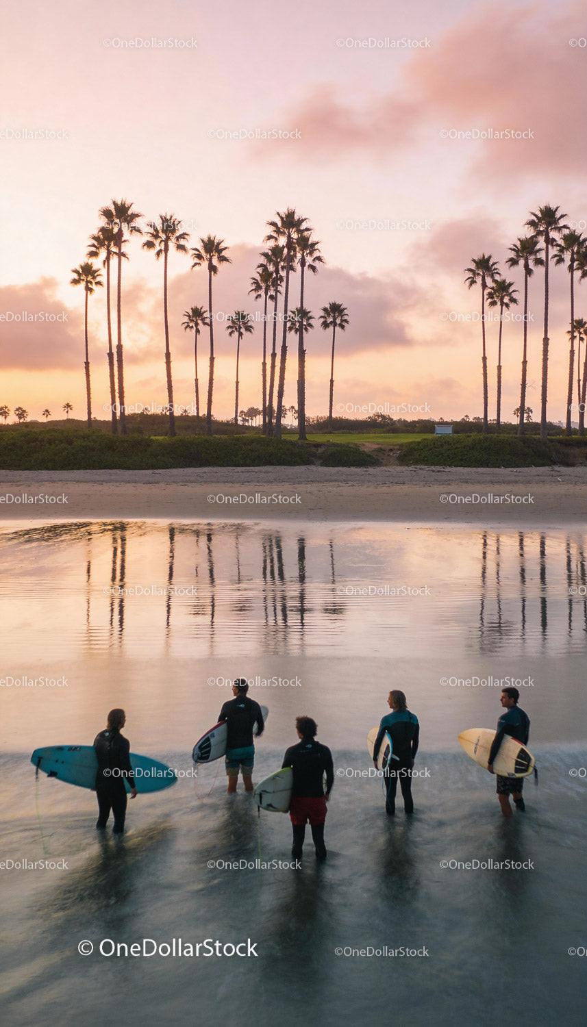 Group of surfers entering calm waters at sunset