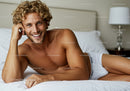 Smiling young man relaxing in bed wearing white underwear