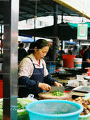 Woman chopping fresh vegetables at busy market stall