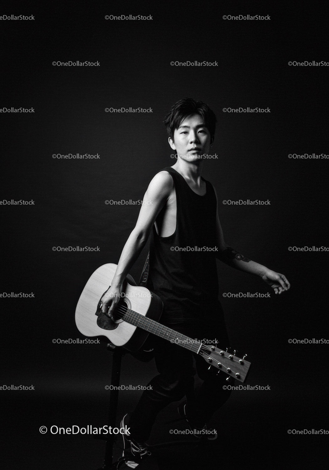 Young man holding acoustic guitar in dark studio